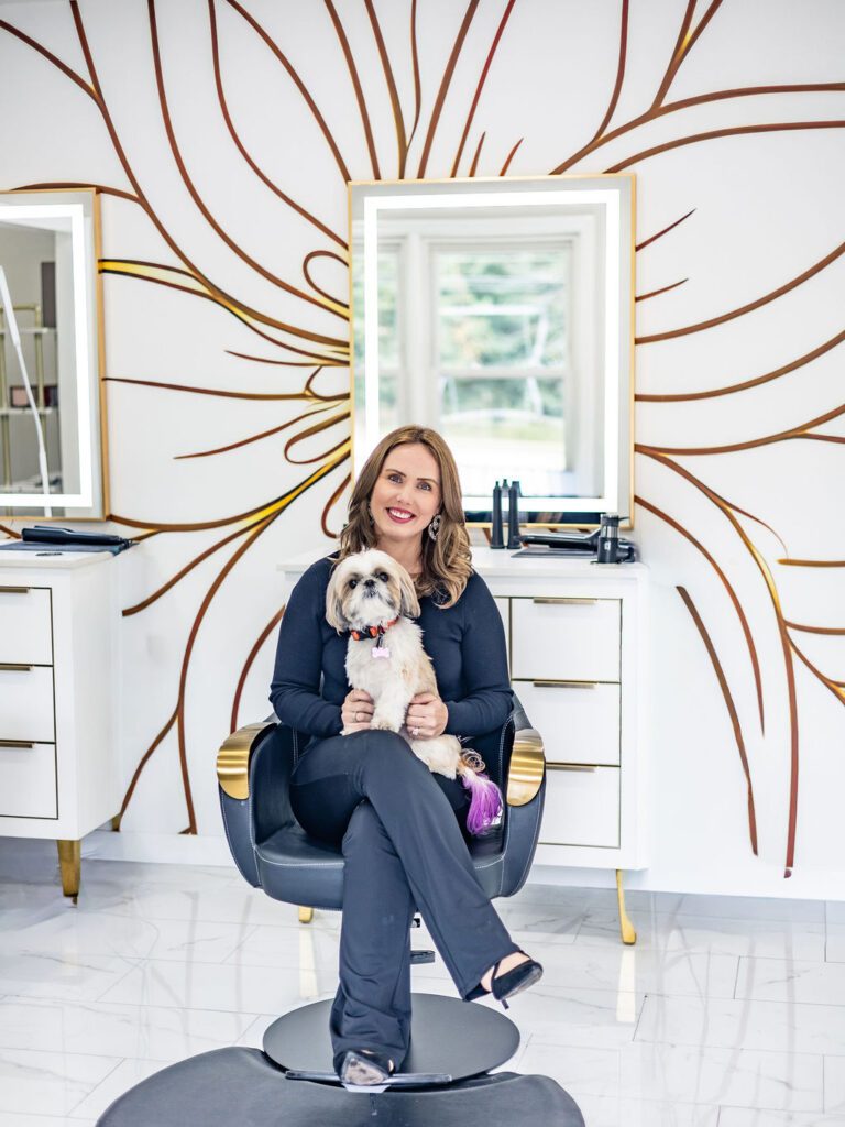 Woman sitting with dog in salon chair.